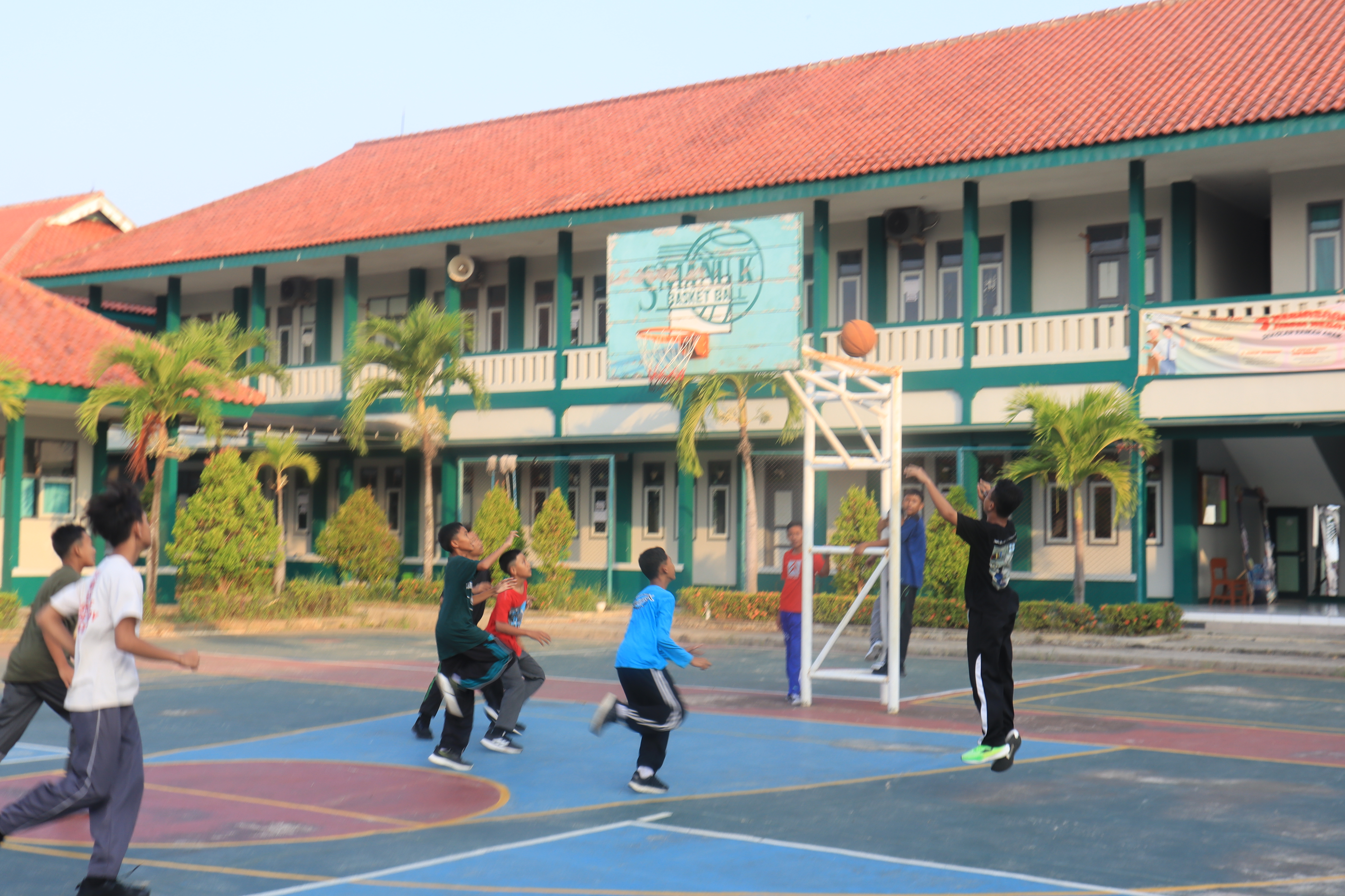 Santri bermain basket di lapangan outdoor dengan gedung sekolah